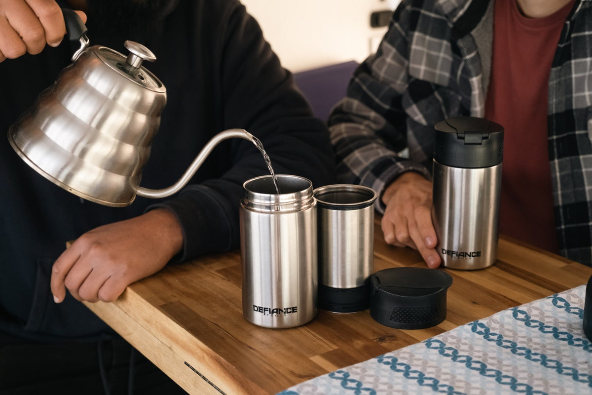 Person pouring coffee from a kettle into an insulated French Press on a wooden table.