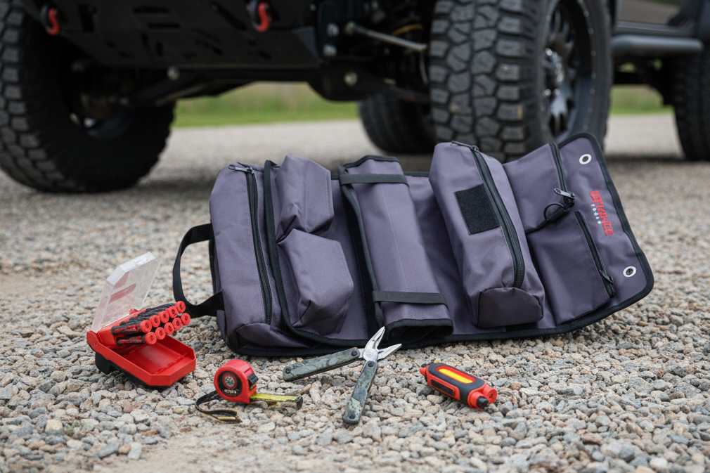 Tool bag with tools on a gravel surface next to a vehicle